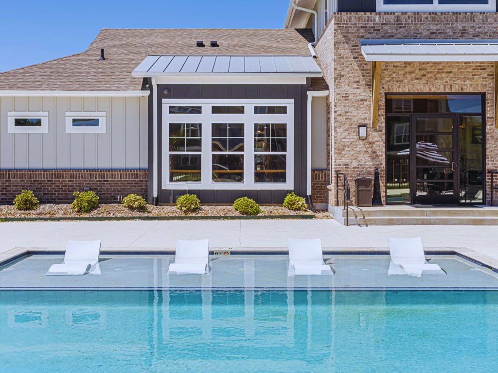a swimming pool in front of a house with a pool and chairs