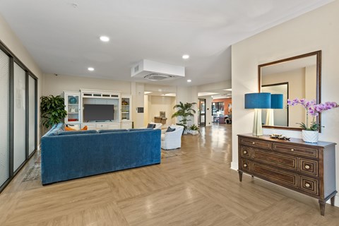 A blue couch sits in a spacious living room with a wooden floor and a large mirror on the wall.