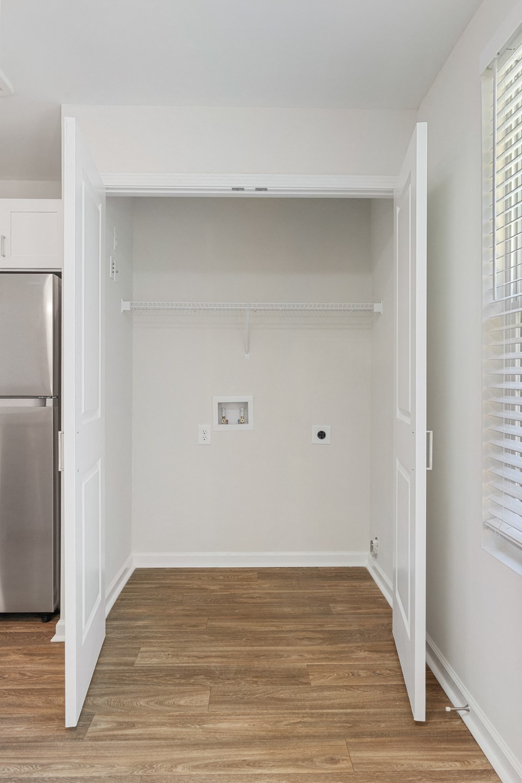 an empty room with white walls and wood floors and a refrigerator