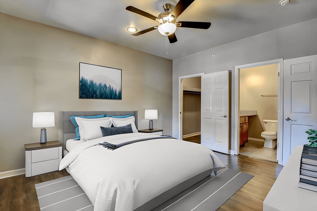 A bedroom with a large bed, a ceiling fan, and a painting of a forest on the wall.
