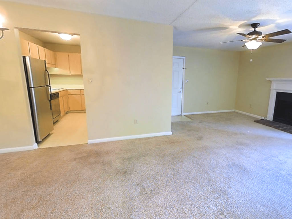 an empty living room with a kitchen and a ceiling fan