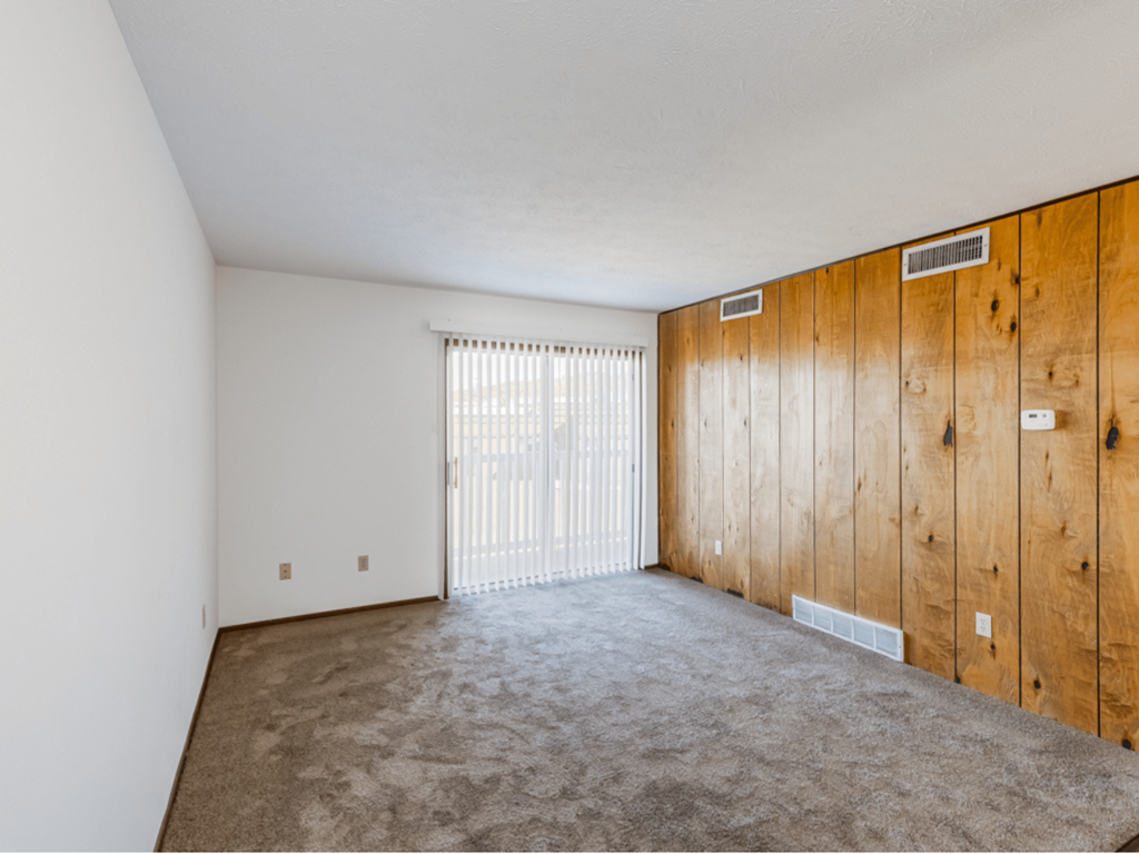 an empty living room with a wooden wall and a sliding glass door