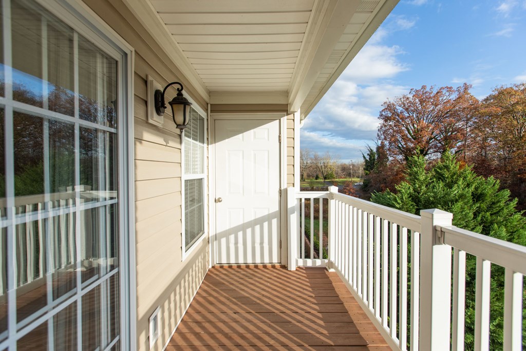 A porch with a white railing and a lamp on the wall.
