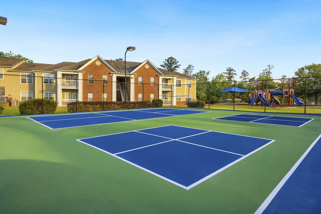a blue and green tennis court with yellow apartments in the background