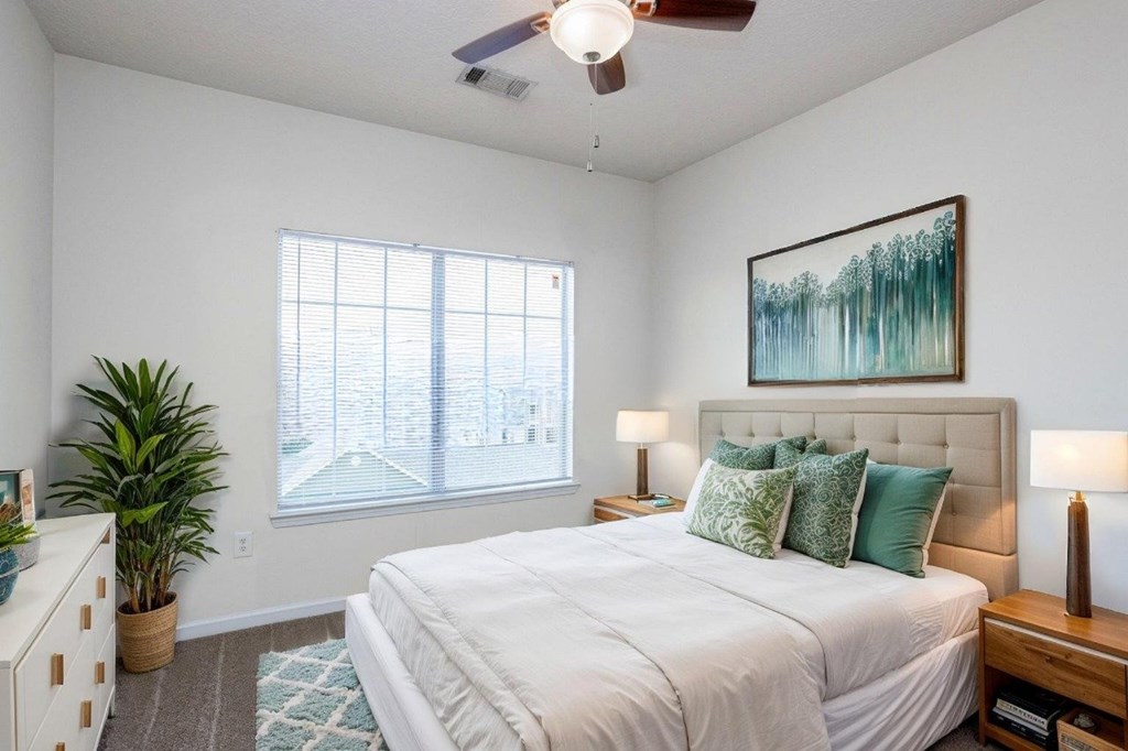 A bedroom with a large bed, a ceiling fan, and a painting on the wall.