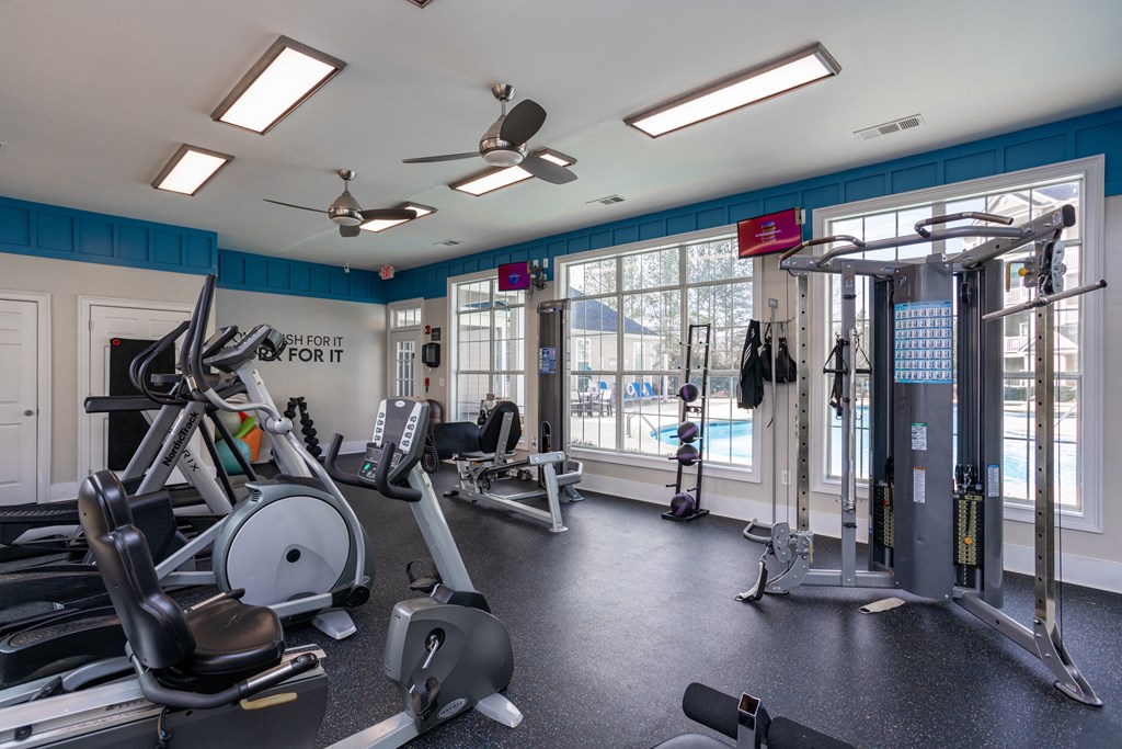 a gym with cardio equipment and windows with a view of a pool