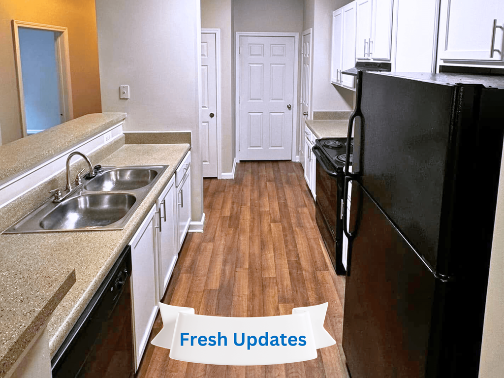 A kitchen with a black fridge and a sink with a granite counter top.