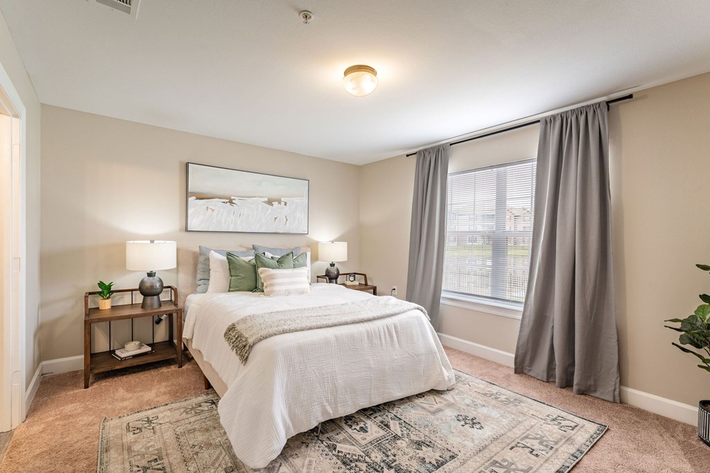 A bedroom with a large bed and a window with curtains.