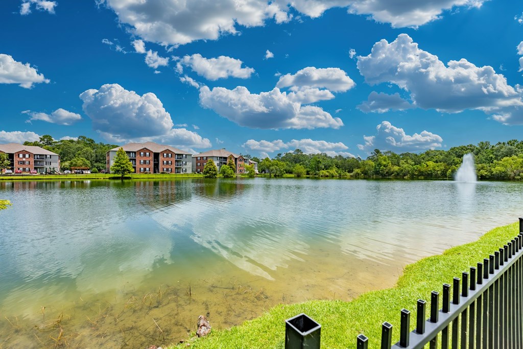 A serene lake with a fountain in the distance and apartment buildings in the background.