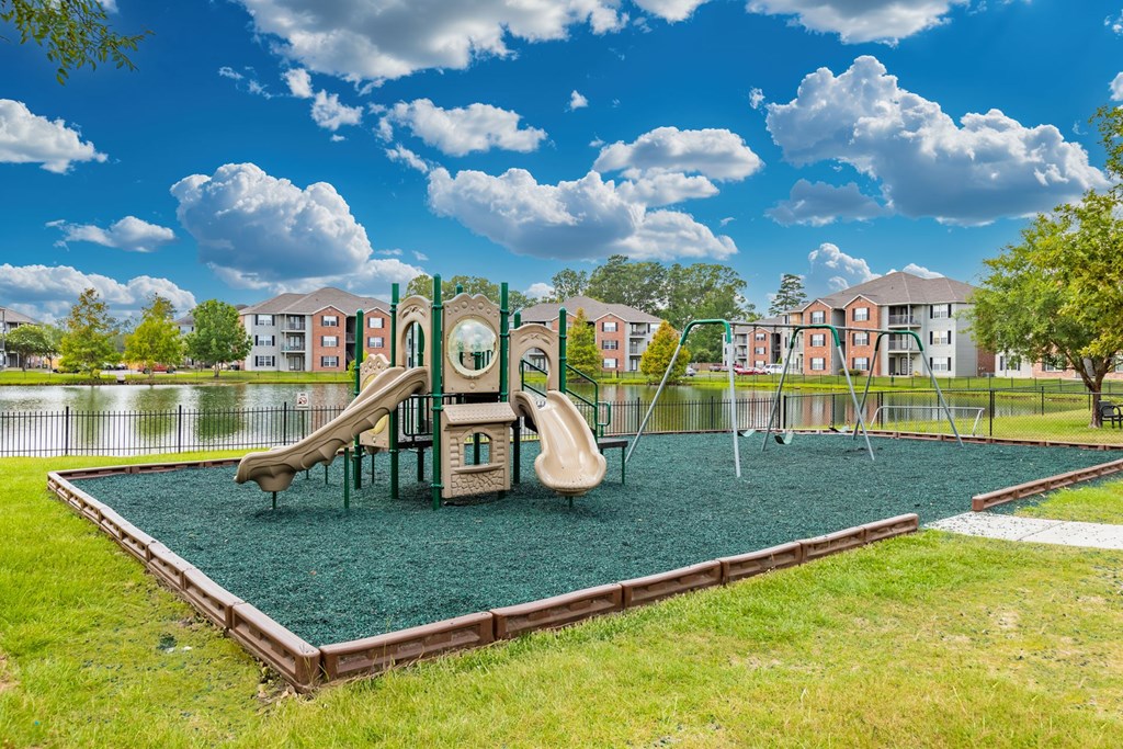 A playground with a green slide and a brown swing set.