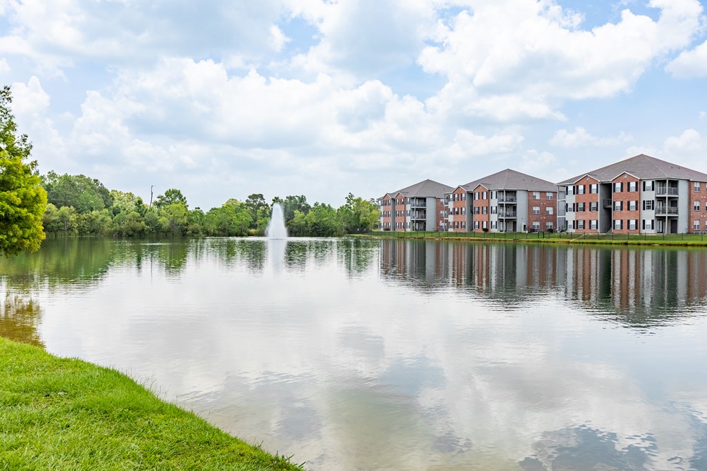 A serene lake with a fountain in the middle and apartment buildings in the background.