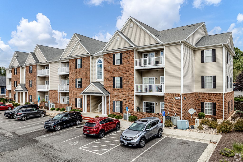 A parking lot in front of a multi-story apartment building with cars parked.