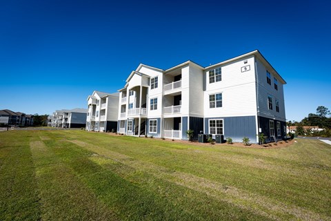 A large white building with a blue trim is surrounded by a grassy field.