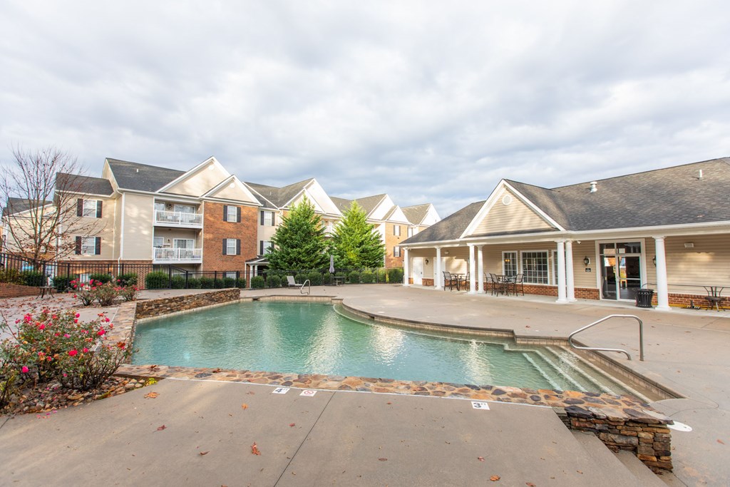 A swimming pool in front of a building with a patio and chairs.