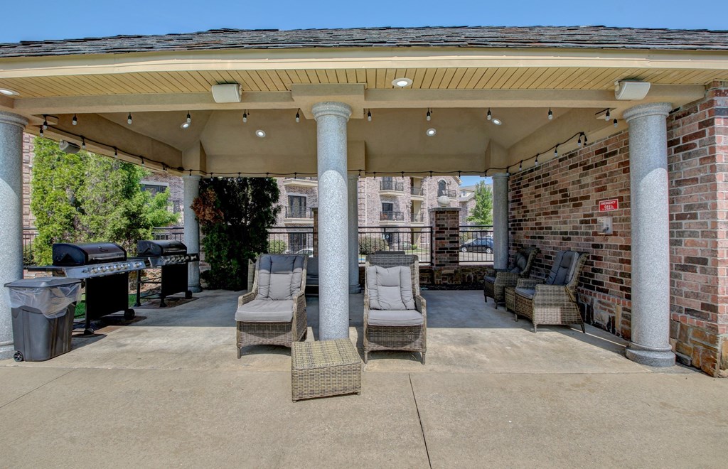 A covered patio area with chairs and a grill.