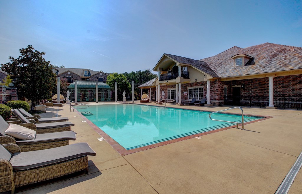 A large outdoor swimming pool surrounded by lounge chairs and a building in the background.