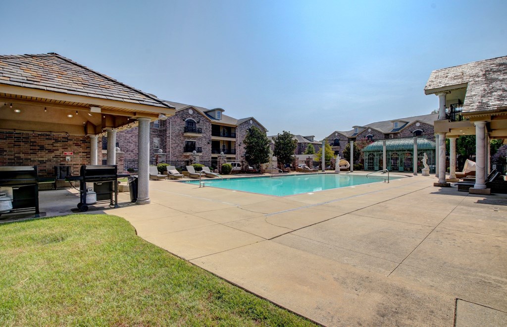 A large outdoor swimming pool surrounded by a concrete patio and a covered seating area.