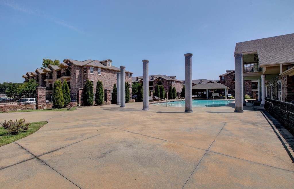A concrete patio with four pillars in the middle and houses in the background.