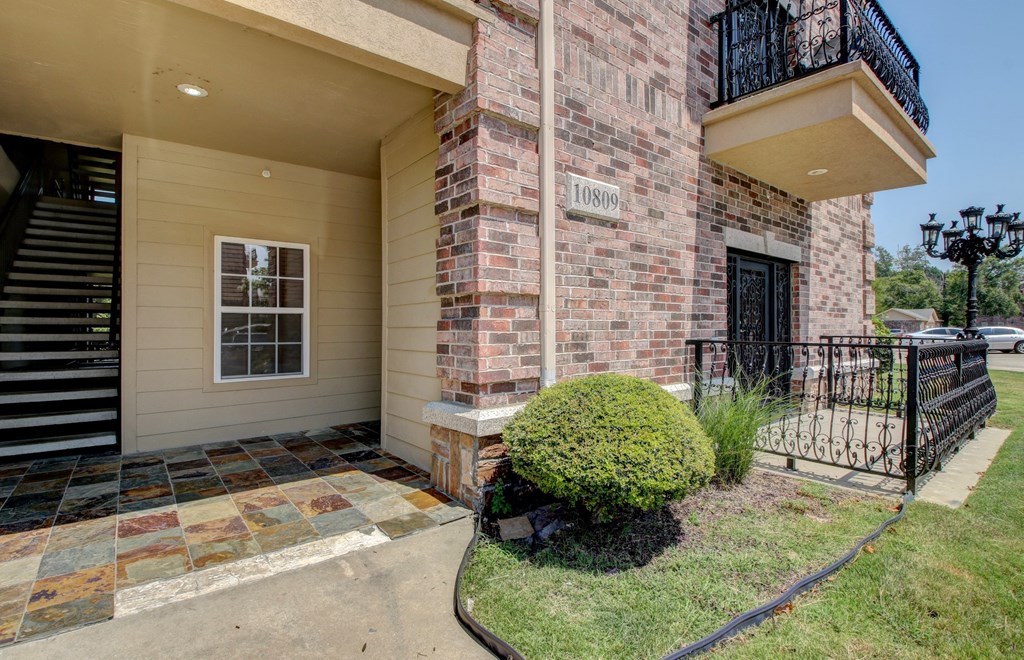 A brick building with a black gate and a green bush in front.