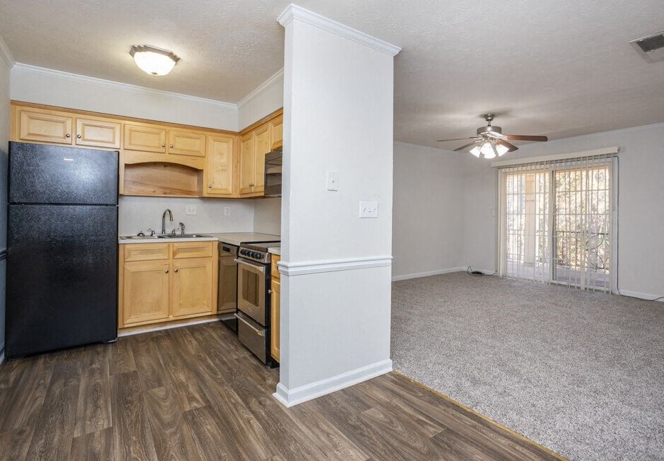 an empty living room with a kitchen and a ceiling fan