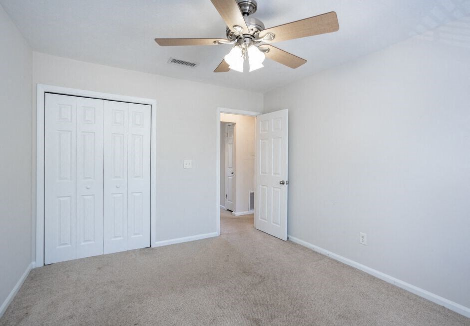 an empty living room with a ceiling fan and a closet
