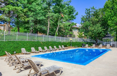 A pool surrounded by chairs and trees.