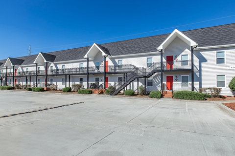 A parking lot in front of a white building with red doors.