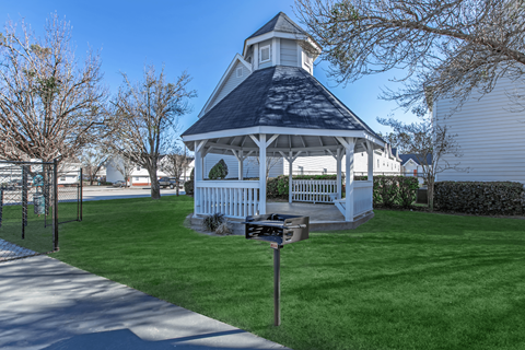 A white gazebo with a black roof is surrounded by a green lawn.