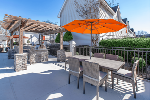 A patio with a table and chairs under a large orange umbrella.
