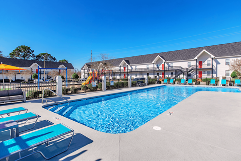 A large swimming pool with sun loungers and a playground in the background.