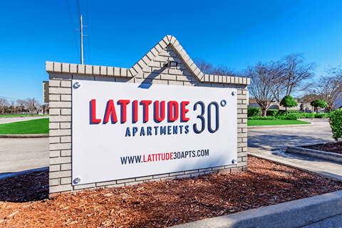 A sign for Latitude 30 Apartments is displayed in front of a building.