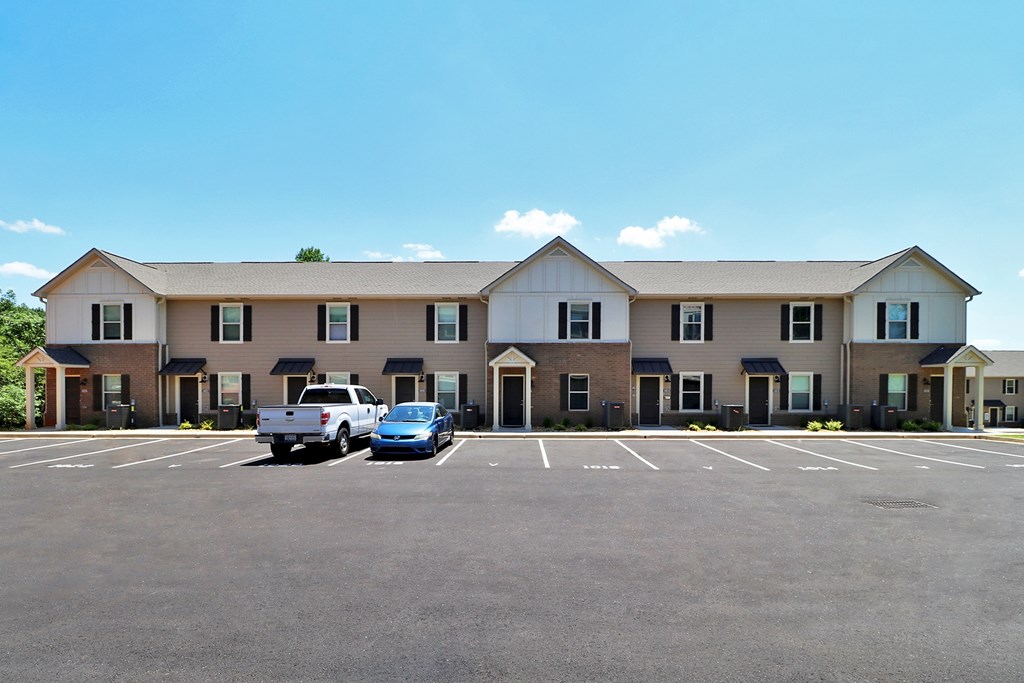 A parking lot in front of a building with a white truck and blue car.