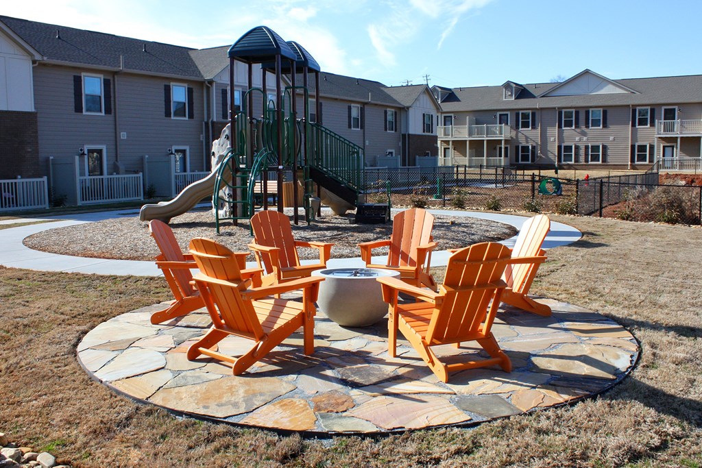 A fire pit surrounded by chairs in a grassy area.