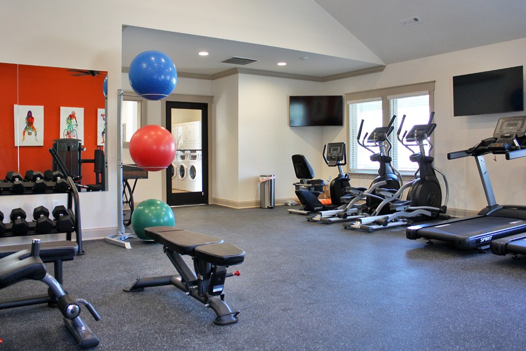 A gym with a variety of equipment including treadmills, weights, and exercise balls.