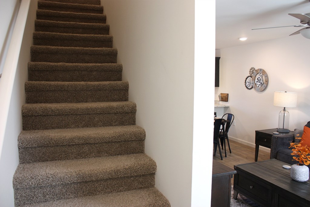 A staircase with a carpeted runner and a fan in the room.