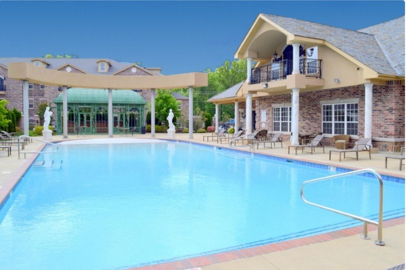 A large swimming pool in front of a building with a balcony.