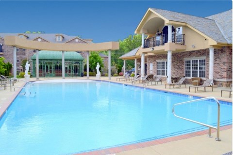A large swimming pool in front of a building with a balcony.