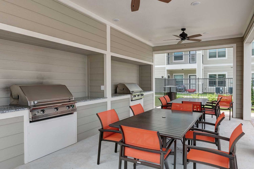 a covered patio with a table and chairs and a grill