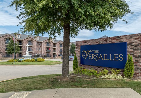 a sign for the versailles on the side of a brick building with a tree