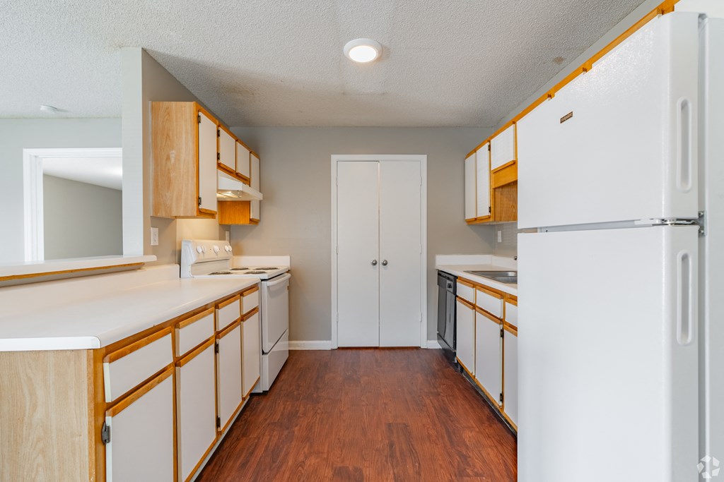 a kitchen with white counters and wooden cabinets and a refrigerator
