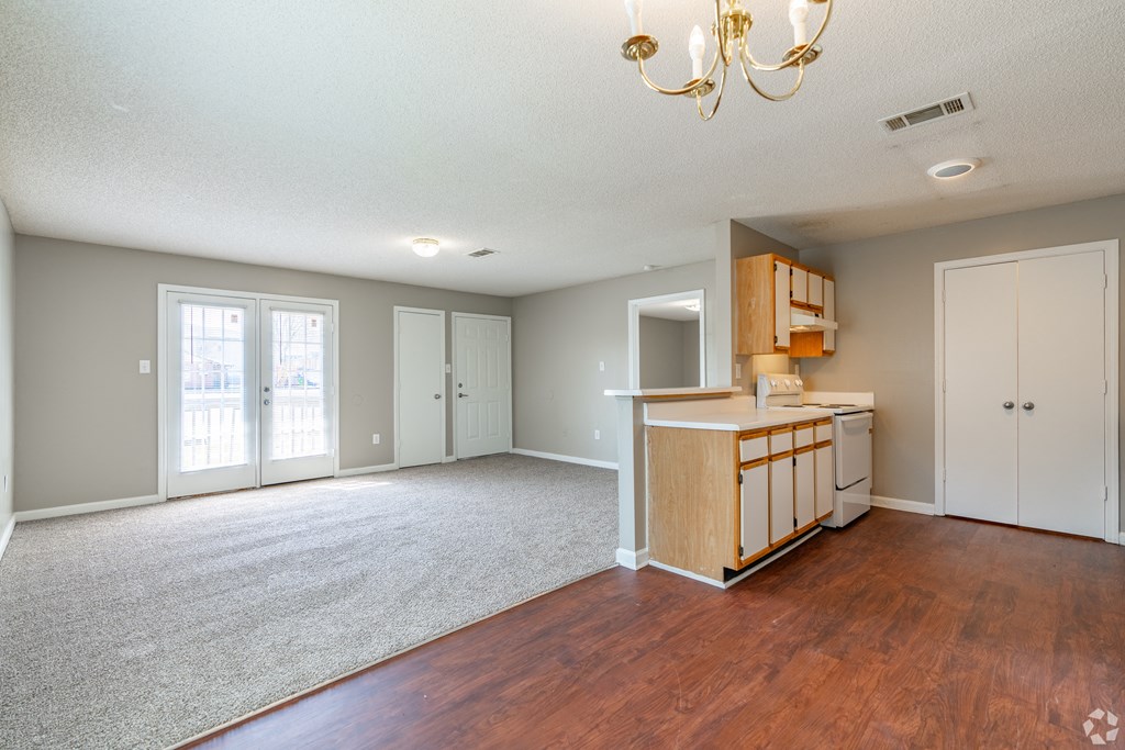 an empty living room with a kitchen and a chandelier