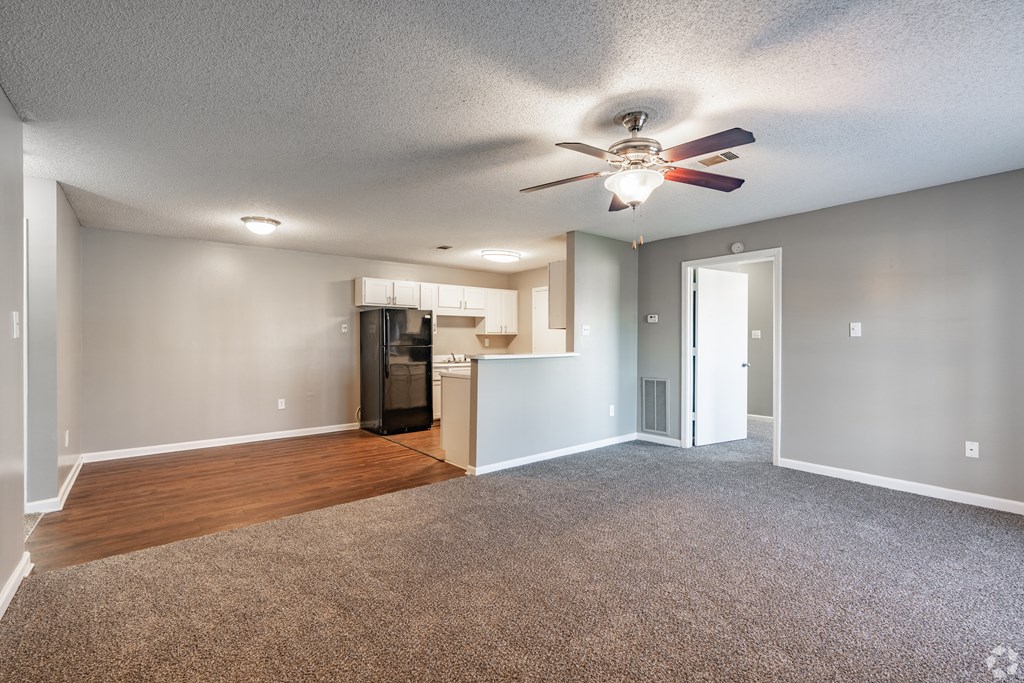 an empty living room with a ceiling fan and a kitchen