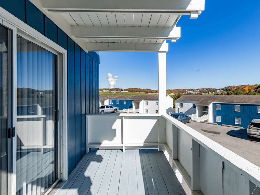 a covered balcony with a view of a parking lot and blue buildings