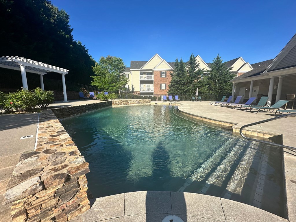 A pool with a stone wall and a building in the background.