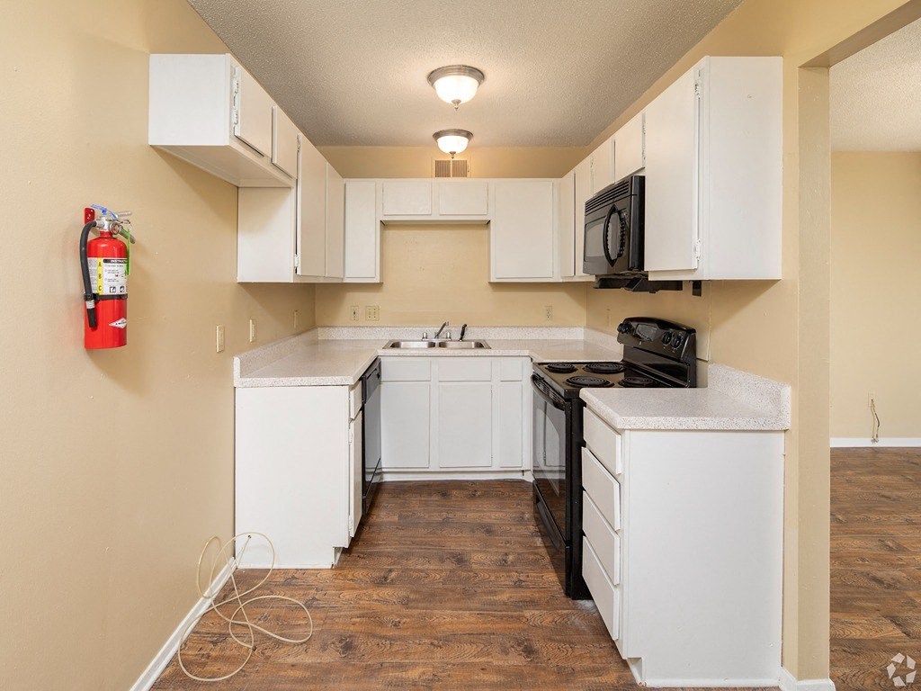 an empty kitchen with white cabinets and a black stove and a fire extinguisher