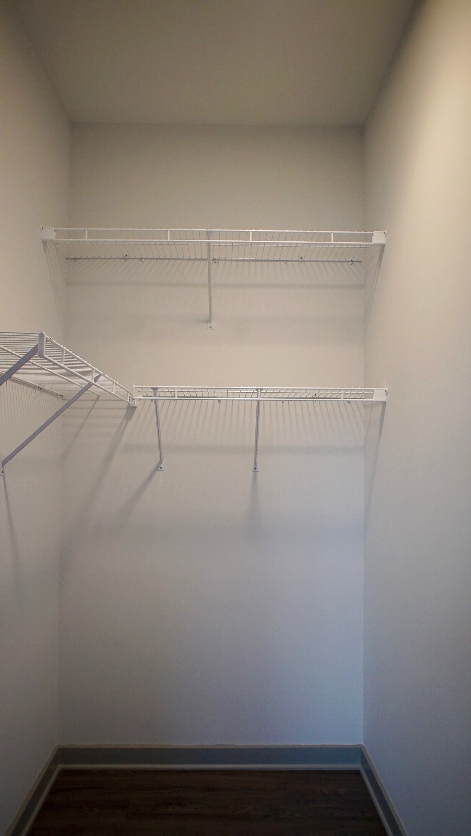 a walk in closet with a white wall and a white shelf on top of it