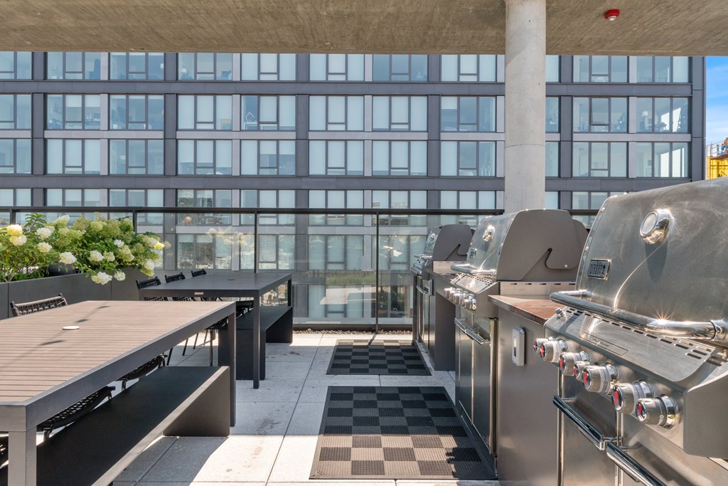 an outdoor patio with barbecue grills and picnic tables with a large building in the background