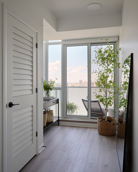 A white door opens to a balcony with a view of the city.