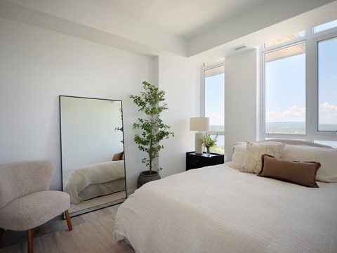 A bedroom with a large bed, a chair, a mirror, and a potted plant.