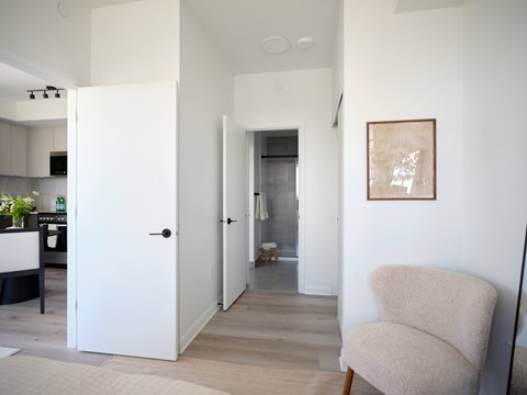 A white chair sits in a hallway with a white door and a picture on the wall.